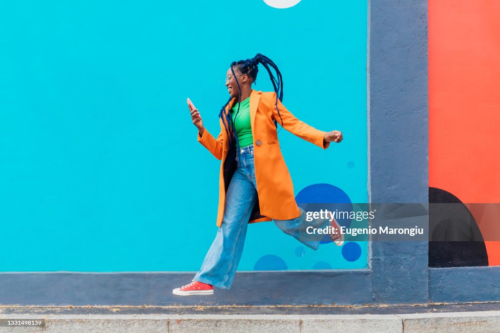 Italy, Milan, Woman with braids jumping against blue wall