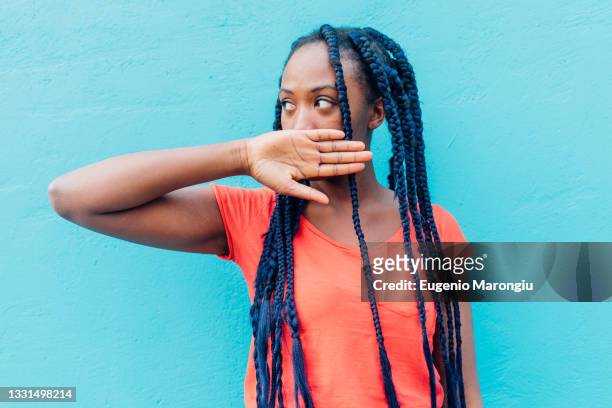 italy, milan, young woman covering mouth in front of blue wall - woman hush stock pictures, royalty-free photos & images