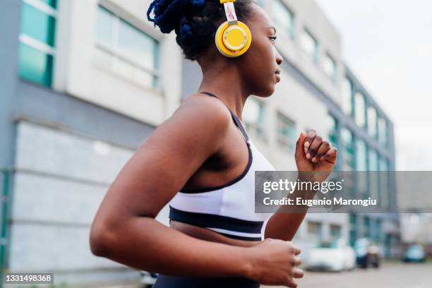 italy, milan, woman with headphones jogging in city - sportbeha stockfoto's en -beelden