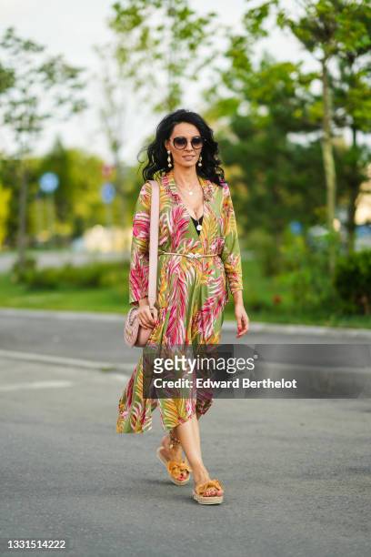 Cosmina Pasarin wears sunglasses, long pearl earrings, a green and pink floral print low-neck flowing dress, a pink quilted Moschino bag, ankle...