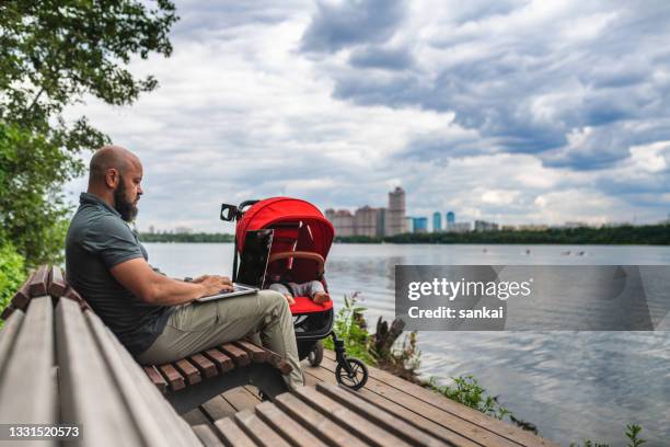 reifer mann mit laptop, der im freien in einem öffentlichen park mit schlafendem baby im kinderwagen arbeitet, home-office-konzept - riverbank stock-fotos und bilder