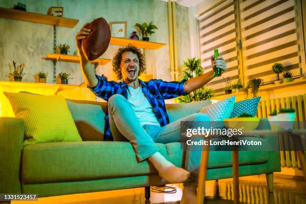 giovane uomo felice che guarda il football americano in tv - afl ball foto e immagini stock