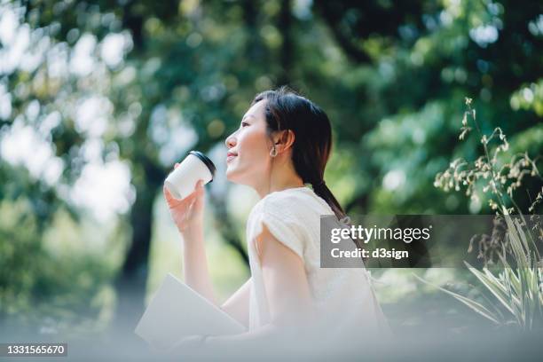 young asian woman sitting on a bench in park, reading a book and having a relaxing time enjoying the sunny day outdoors in the city. enjoying a technology-free moment - mujer leyendo libro en el parque fotografías e imágenes de stock