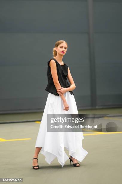 Denisa Corb wears a black sleeveless flowing t-shirt, a white long asymmetric flowing midi skirt, black shiny open toe-cap / strappy pumps heels...