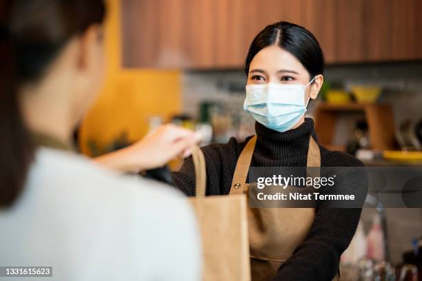 safety is essential for customers. shot of asian women barista handing takes away food and drinks in a paper bag to her customers in a coffee shop. food ordering, takeaway, point of sale system. - carry on bag bildbanksfoton och bilder