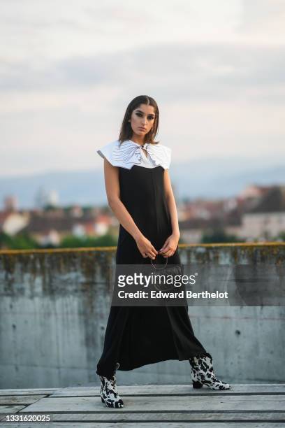 Jacqueline Barth wears a black long tube slit / split dress with a white epaulets collar with a drawing of two women's faces, a black shiny quilted...