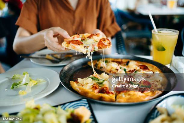 close up of young asian woman getting a slice of freshly made pizza. enjoying her meal in restaurant. italian cuisine and culture. eating out lifestyle - carbohidrato fotografías e imágenes de stock