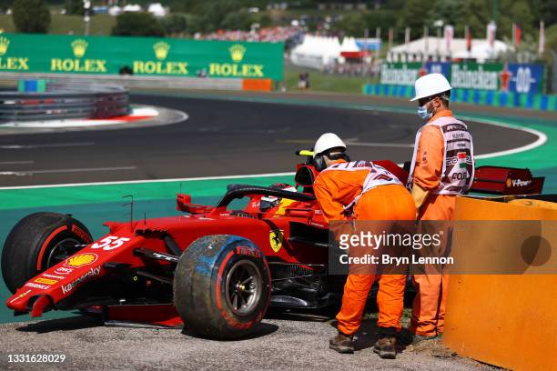 Track marshals talk with Carlos Sainz of Spain and Ferrari as he tries to get his car started again after a crash during qualifying ahead of the F1...