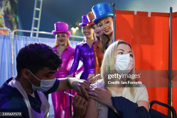 Rhiannon Alexander from Bradford receives a Covid 19 vaccination as circus performers look on during a staged photo at a new ‘Pop Up’ vaccination...