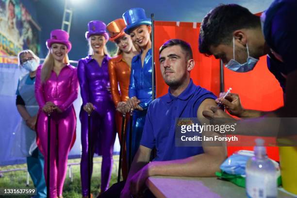 Circus lighting technician Ryan Dobie receives a Covid 19 vaccination as circus performers look on during a staged photo at a new ‘Pop Up’...