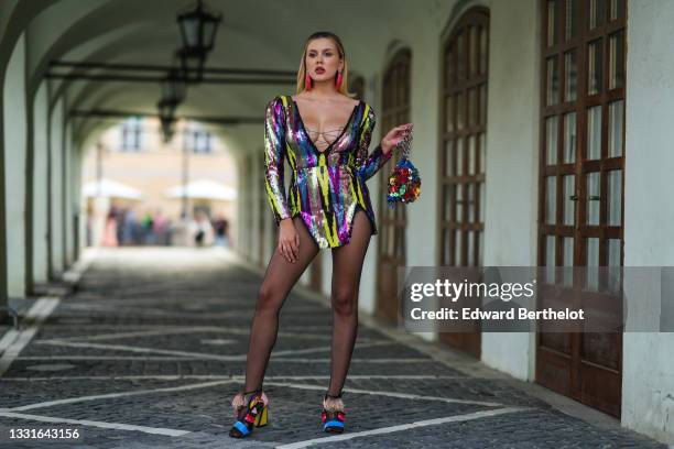 Emily Burghelea wears silver and pink shell pendant earrings, a black / yellow / green / pink / blue / purple sequins print pattern long sleeves /...