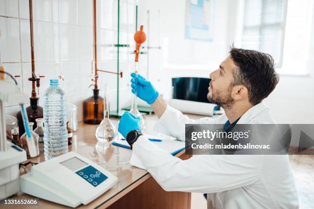 smiling chemist pouring water into the test tube while standing in the lab. water quality check concept. - voedselveiligheid stockfoto's en -beelden