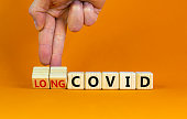 Long covid symbol. Doctor turnes wooden cubes and changes words 'covid' to 'long covid'. Beautiful orange background, copy space. Medical, covid-19 pandemic long covid concept.