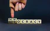 Democracy or autocracy symbol. Businessman turns wooden cubes and changes the word autocracy to democracy. Beautiful grey background, copy space. Business and democracy or autocracy concept.