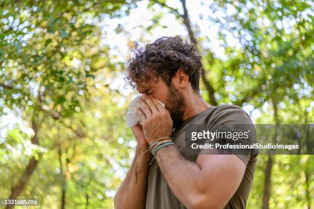 a man with flu is walking in public park and sneezing in paper tissues. - season stock pictures, royalty-free photos & images