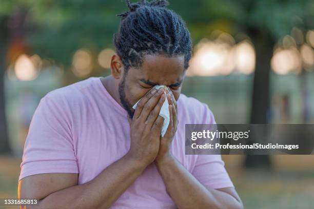 allergic african man is blowing his nose in the park. - covering nose stock pictures, royalty-free photos & images