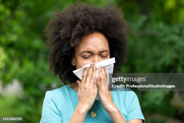 young african woman with cold or flu is blowing her nose in public park. - cold virus stock pictures, royalty-free photos & images