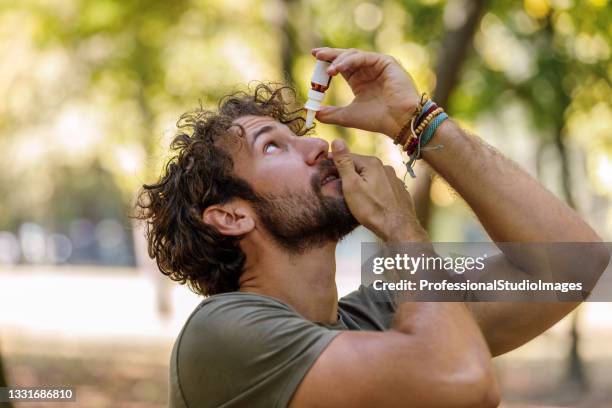 a mature man with eye problems is applying eye drops in nature. - allergie stockfoto's en -beelden