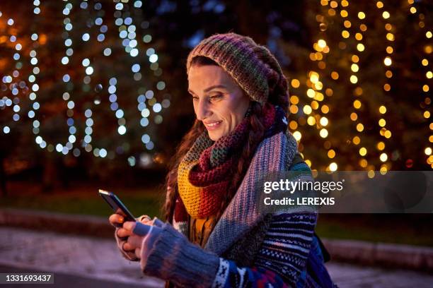 woman uses a mobile phone against the backdrop of christmas decorations - kerstboom versieren stockfoto's en -beelden