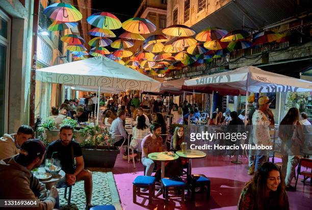 Tourists and locals sit at sidewalk tables under rainbow umbrellas in Pink Street, Cais do Sodre, on the night before 11pm traffic restrictions end...