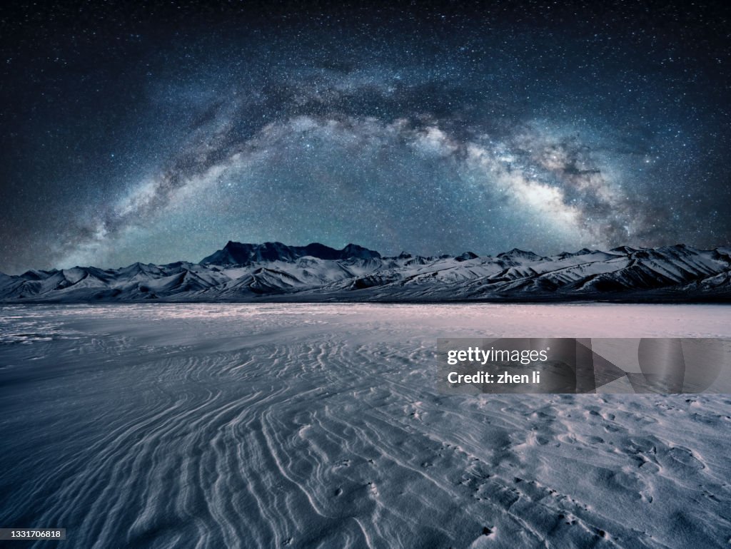 Snowcapped mountain and flat snowfield under the galaxy arch bridge