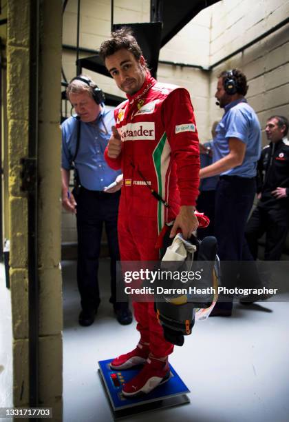 Spanish Scuderia Ferrari Formula One team racing driver Fernando Alonso standing on the FIA Parc Fermé weight scales while holding his crash helmet,...