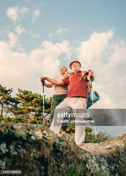 photo of an elderly couple during their hike with backpacks, reached the top of the mountain - senior women hiking stock pictures, royalty-free photos & images