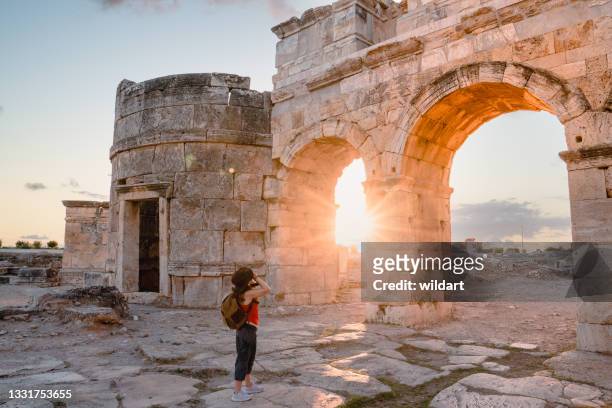 photographer tourist girl is taking photos of the frontinus gate in ancient ruins in hierapolis , pamukkale - oude ruïne stockfoto's en -beelden