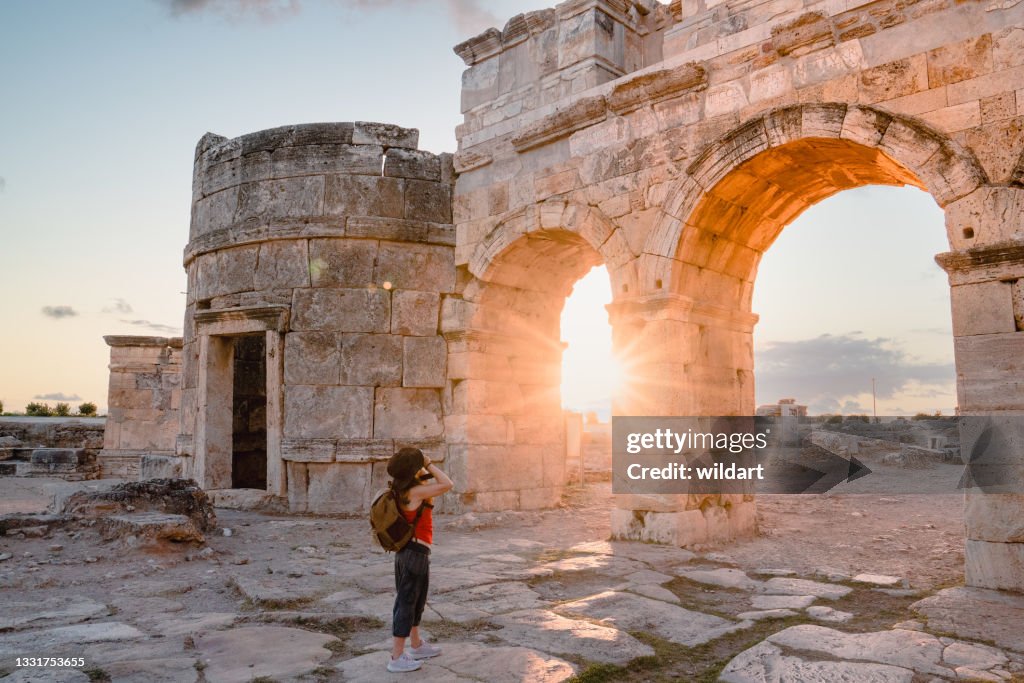 Photographer tourist girl is taking photos of the Frontinus Gate in ancient ruins in Hierapolis , Pamukkale