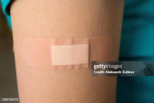 a band-aid or adhesive bandage on the arm of a girl or young woman, after vaccination or injection. the concept of medicine and health care, vaccination and treatment of diseases. first aid. - needle injury stock pictures, royalty-free photos & images