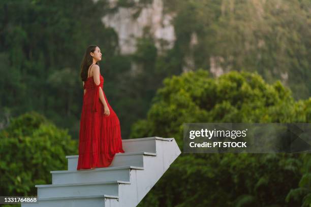 a woman dressed in red sits on a white stairway surrounded by mountains. - budding starlets stock-fotos und bilder