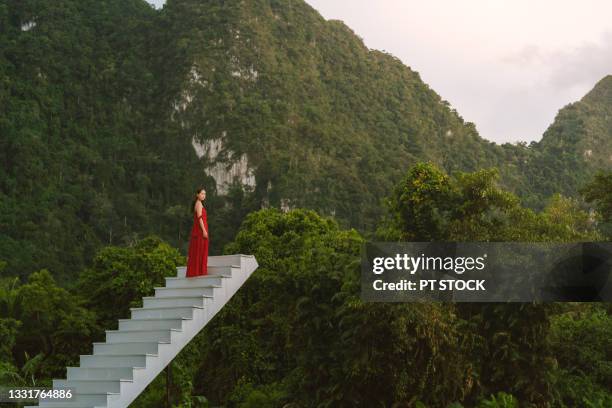 a woman dressed in red sits on a white stairway surrounded by mountains. - best bosom fotografías e imágenes de stock