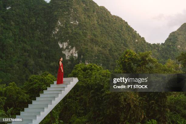 a woman dressed in red sits on a white stairway surrounded by mountains. - glamour asian stock pictures, royalty-free photos & images