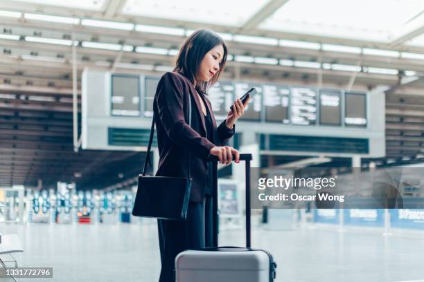 young businesswoman checking in with phone at departure area - viagem de negócios - fotografias e filmes do acervo