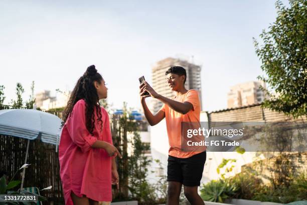 teenager boy using smartphone for filming or taking a picture of sister at home - teen doing filming imagens e fotografias de stock