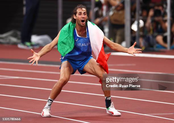 Men's high jump gold medalist Gianmarco Tamberi of Team Italy reacts after watching Marcell Jacobs of Team Italy win the gold medal in the men's 100...