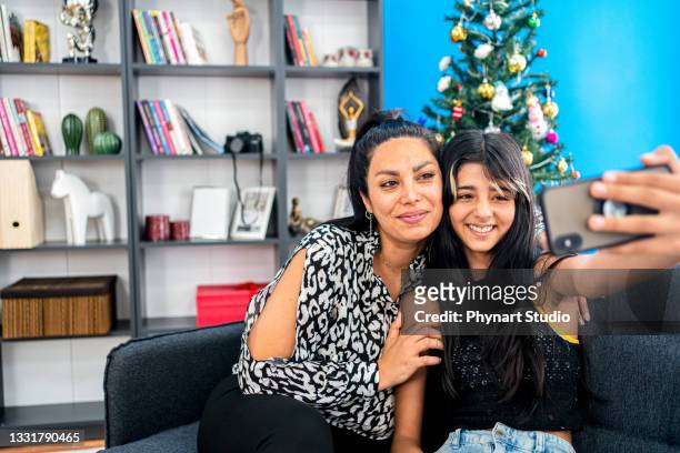 smiling middle eastern mother and daughtertaking selfie on smartphone at home - arab mother and daughter taking selfie imagens e fotografias de stock