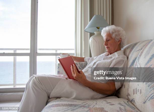 senior woman relaxing on a sofa - book top view stockfoto's en -beelden