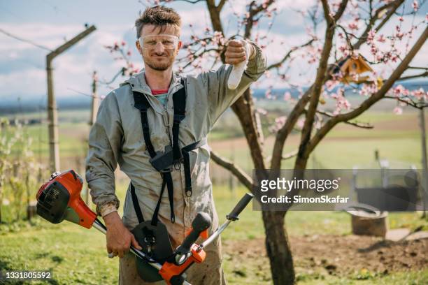 man showing damaged thumbs down while holding weed trimmer - bandaged thumb stock pictures, royalty-free photos & images