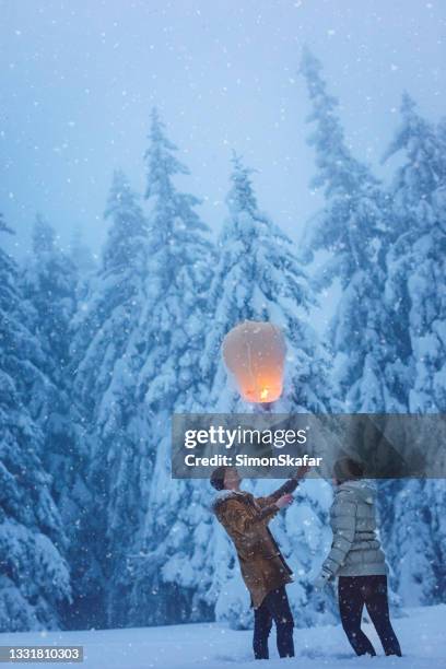 couple releasing paper lantern into sky on snow - releasing lanterns stock pictures, royalty-free photos & images