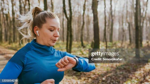 female runner checking smartwatch while running - in ear headphones stock pictures, royalty-free photos & images