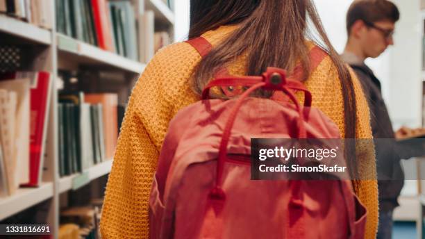 teenage girl searching book through shelves - college preparation stock pictures, royalty-free photos & images