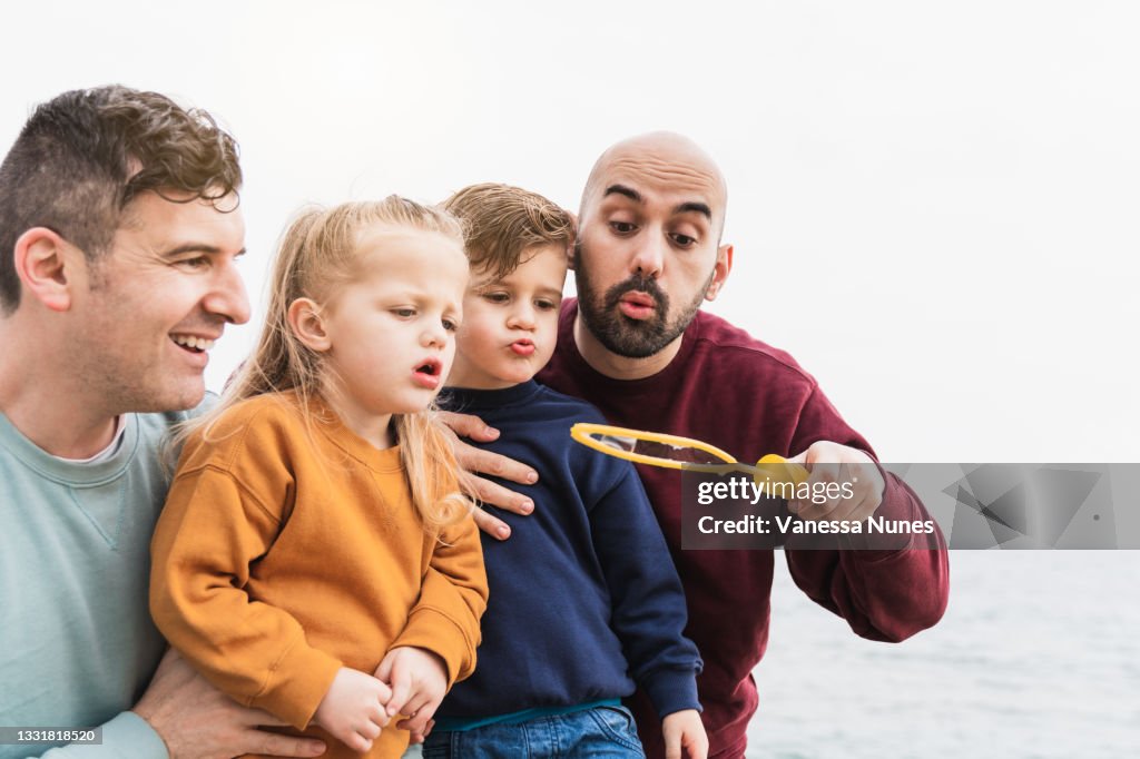Lgbt family having fun with their children at the beach in summer vacation - Gay dads and sons playing together outdoor - Main focus on right man face