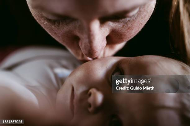 happy mother kissing her thoughtful looking baby girl. - baby and mom fotografías e imágenes de stock