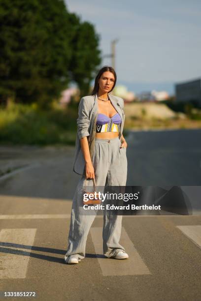 Landiana Cerciu wears a gray oversized blazer jacket with brown / khaki inner lining, purple and yellow black striped cropped top / bras / bralette,...