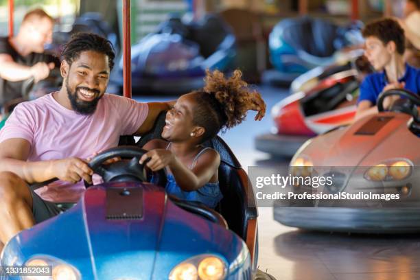 african-american father is driving in bumper car with his cute little daughter. - theme park imagens e fotografias de stock