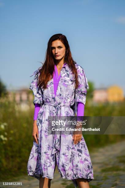 Dariana Cerciu wears an Apoldist full look made of a bold purple bodysuit, a low-neck pastel purple floral print slit dress with integrated belt and...