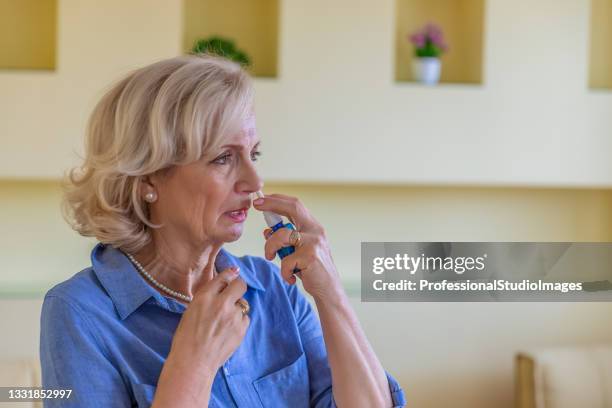 sick senior woman is using nose spray due to allergy or rhinitis. - nose spray stock pictures, royalty-free photos & images