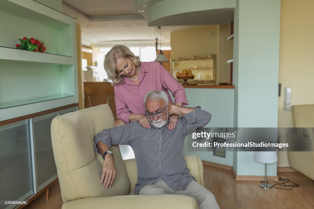 Careful Senior Woman is Helping her Husband with Pain in the Neck.