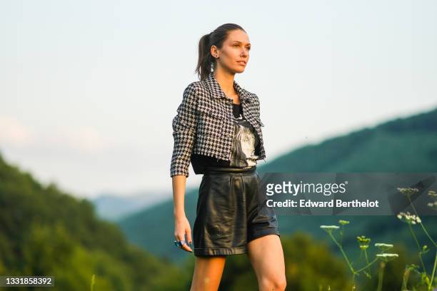 Landiana Cerciu wears a black and white cropped jacket with printed houndstooth patterns, a black and white t-shirt, black leather mini shorts, on...
